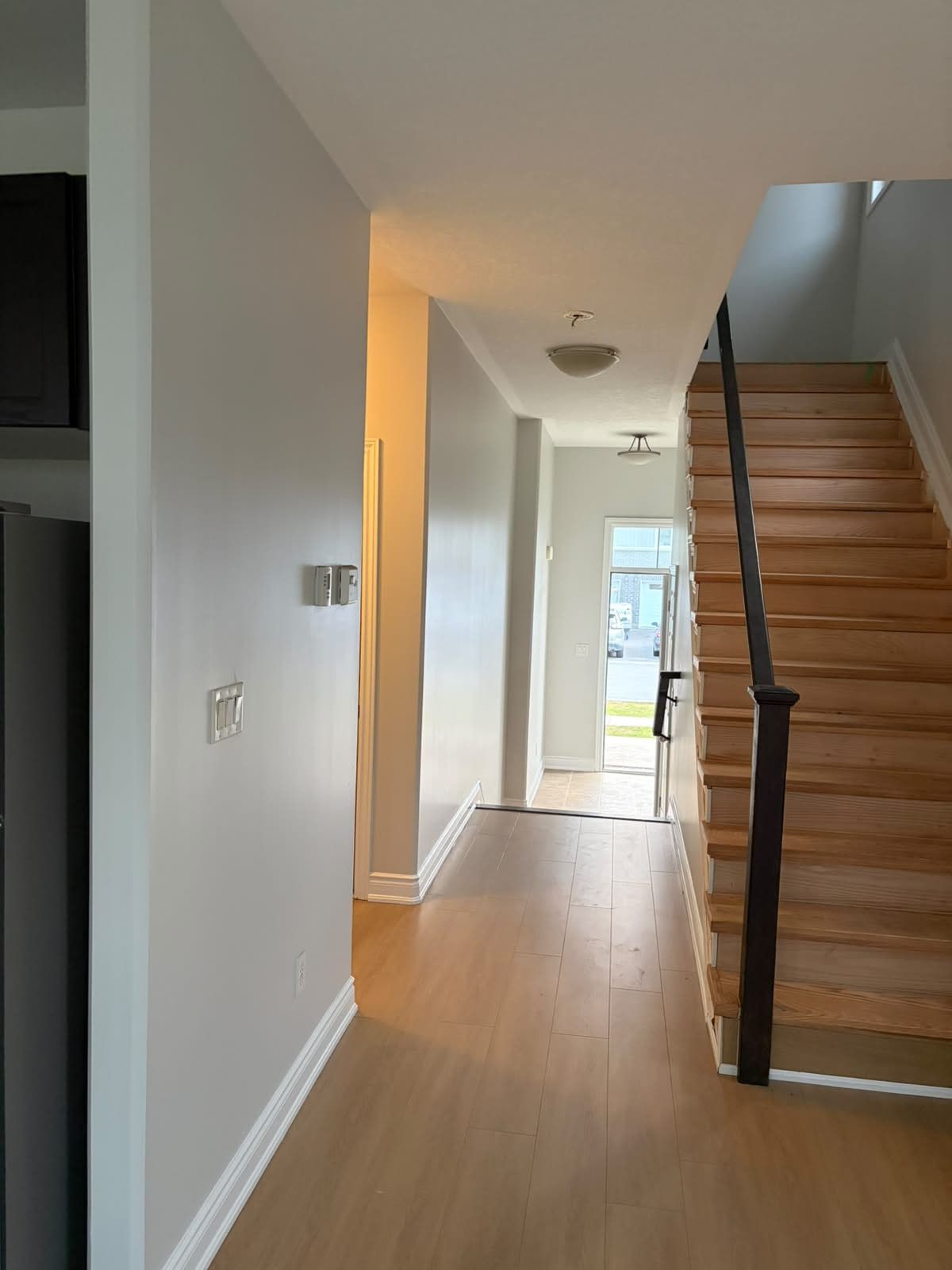 The same front hall after: grey walls, white door and casings, hardwood stairs