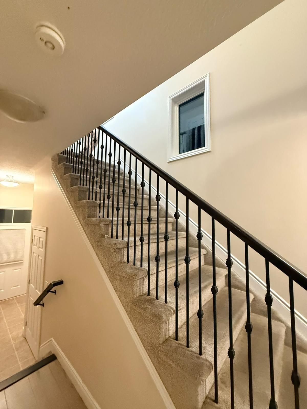 The stairwell before: beige walls, carpeted stairs and a black spindle railing